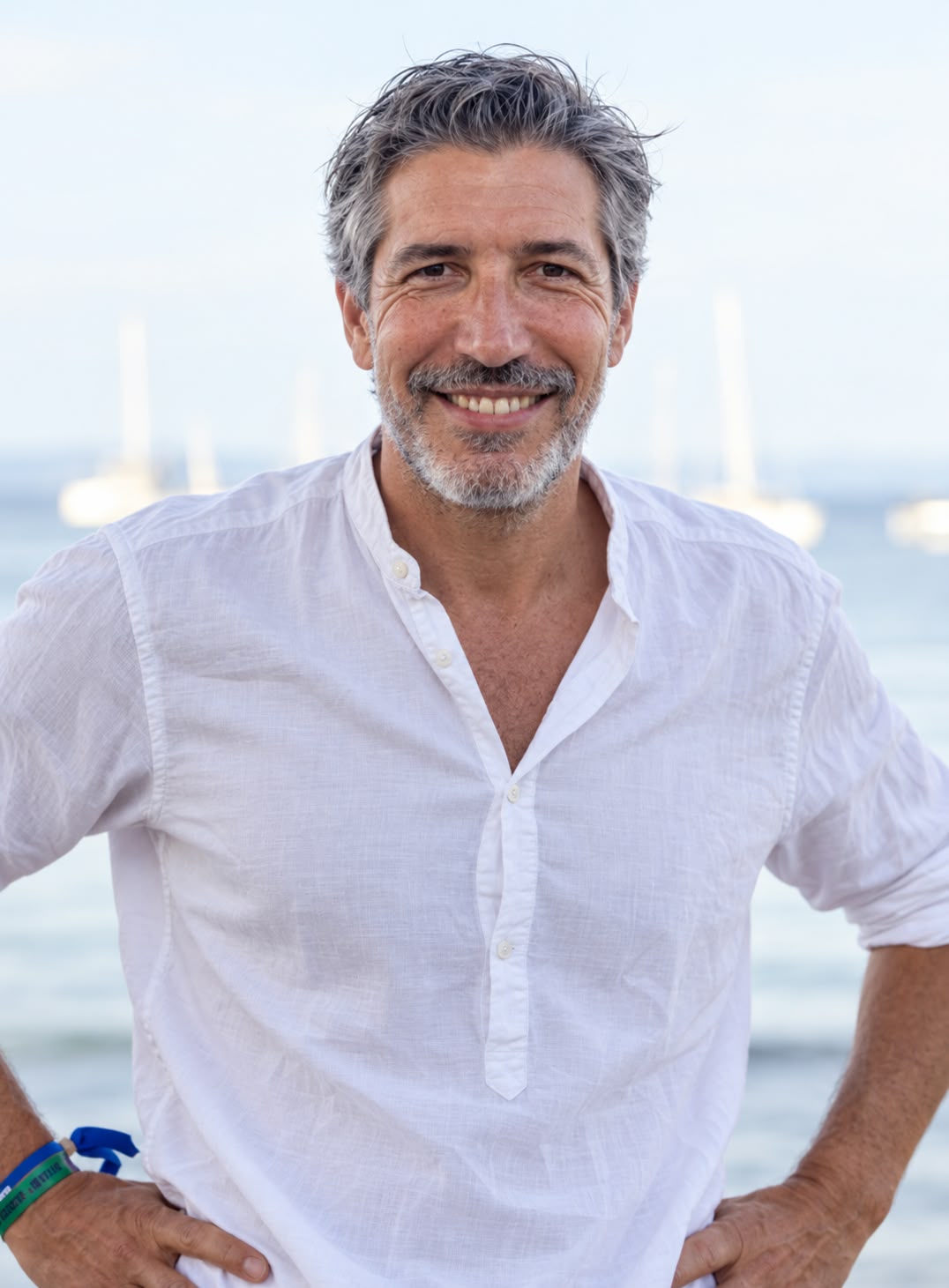 Portrait de Roland Debrabant souriant, en chemise blanche, devant la mer et des voiliers